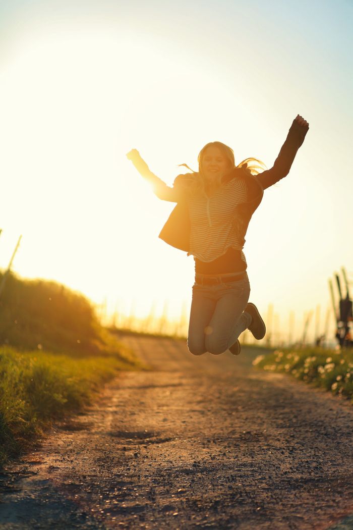 Woman joyfully jumping on a rural path during sunset, embracing freedom and happiness.